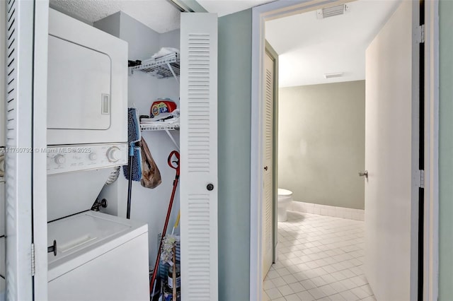 laundry area featuring tile patterned floors, visible vents, stacked washer / drying machine, and laundry area