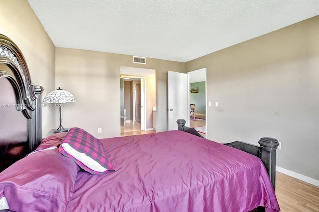 bedroom with baseboards, wood finished floors, visible vents, and a textured ceiling