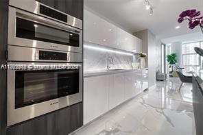 kitchen featuring white cabinetry, double oven, rail lighting, marble finish floor, and modern cabinets