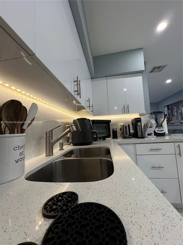 kitchen with visible vents, white cabinets, light stone countertops, and a sink