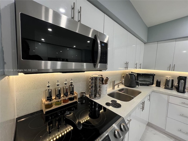 kitchen featuring stainless steel microwave, a sink, decorative backsplash, white cabinetry, and modern cabinets