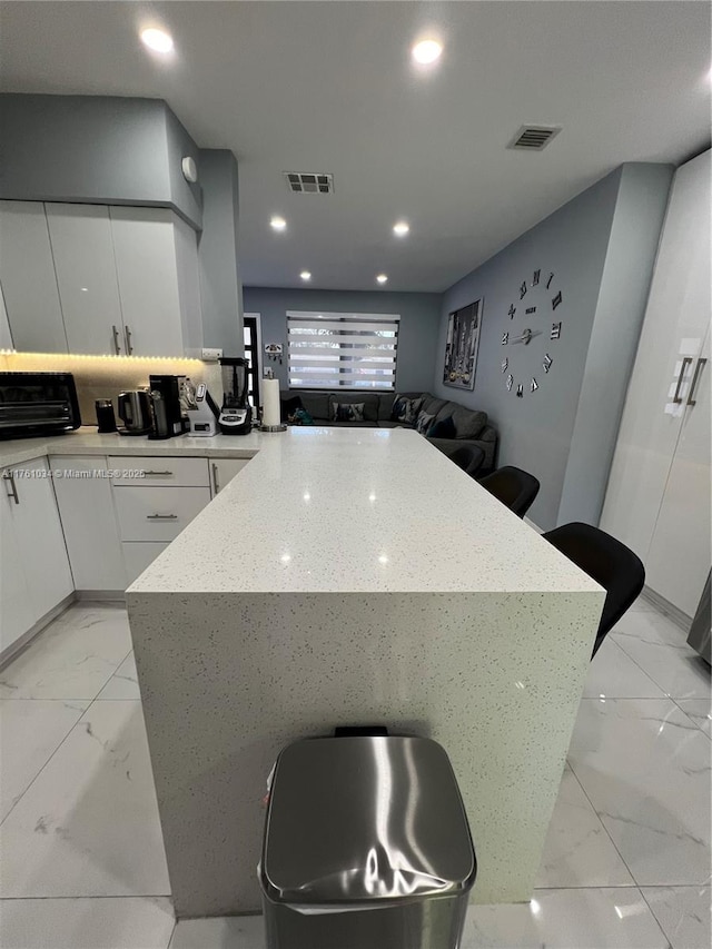 kitchen with visible vents, marble finish floor, white cabinetry, and decorative backsplash