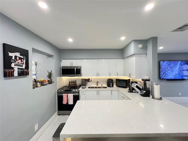 kitchen with light stone countertops, visible vents, a peninsula, a sink, and stainless steel appliances