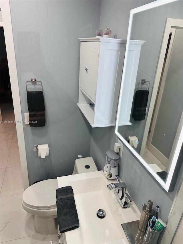 half bathroom featuring marble finish floor, toilet, and a sink