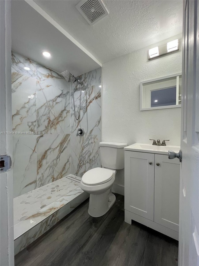 bathroom featuring visible vents, toilet, wood finished floors, a textured wall, and vanity