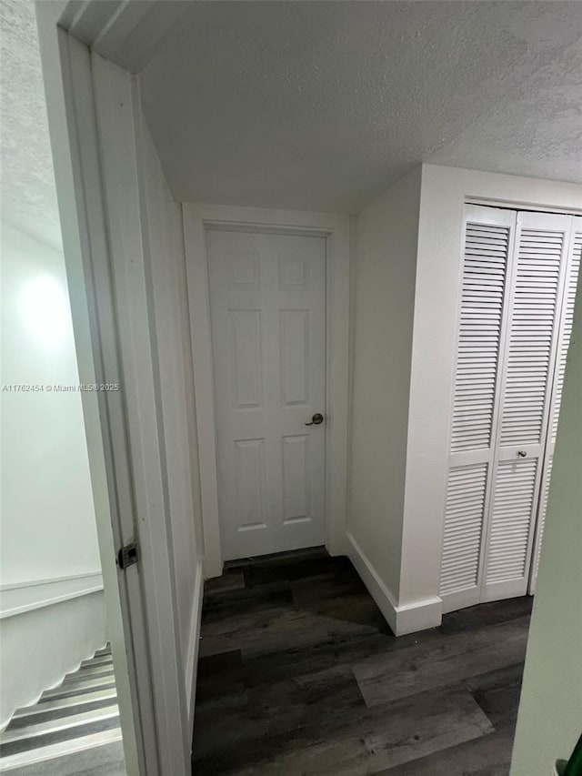 hall featuring baseboards, a textured ceiling, and dark wood-style floors