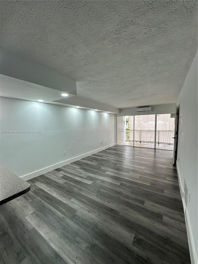 unfurnished room with baseboards, a textured ceiling, an AC wall unit, and dark wood-style floors