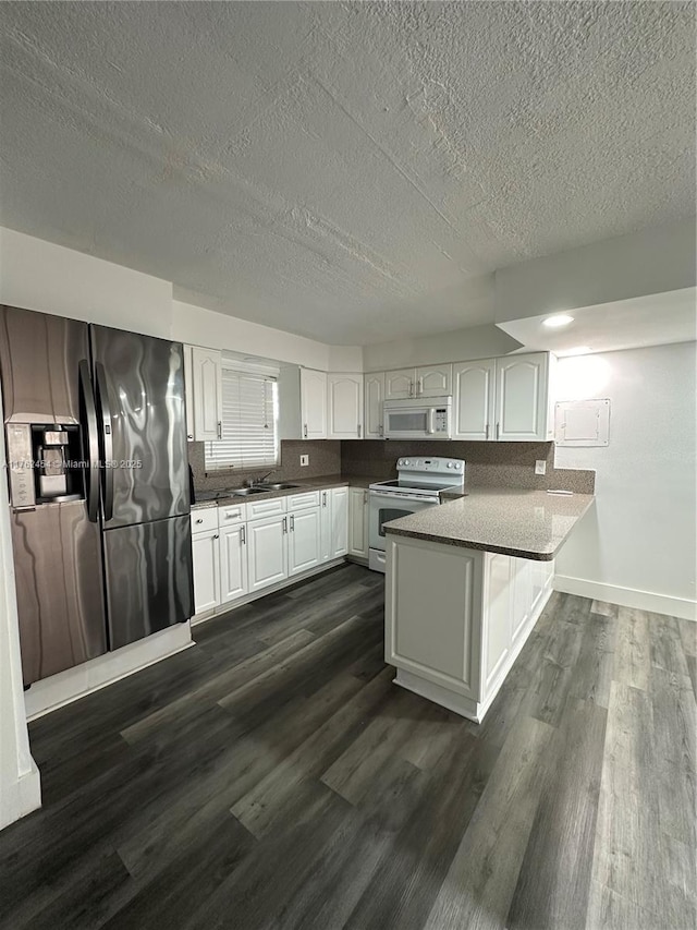 kitchen featuring a sink, dark wood-style floors, white appliances, a peninsula, and white cabinets