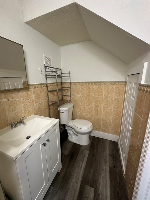 bathroom with toilet, wood finished floors, tile walls, lofted ceiling, and vanity