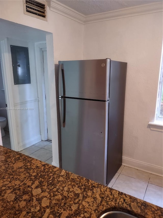 kitchen with light tile patterned floors, visible vents, electric panel, freestanding refrigerator, and ornamental molding