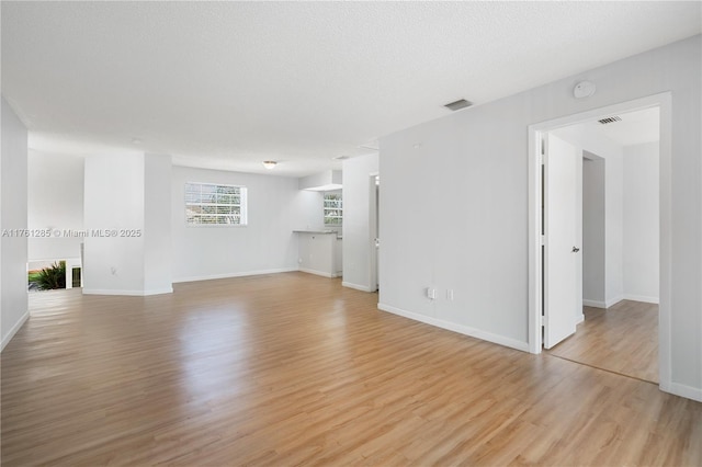 unfurnished living room featuring visible vents, baseboards, a textured ceiling, and light wood-style flooring