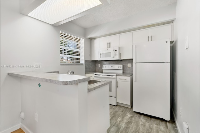 kitchen featuring white appliances, light wood finished floors, a peninsula, decorative backsplash, and white cabinets