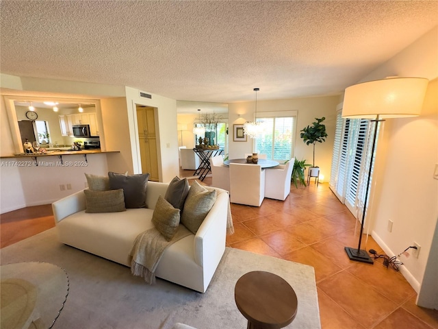 living room featuring visible vents, a textured ceiling, light tile patterned flooring, baseboards, and a chandelier