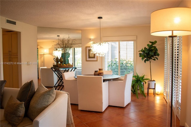 tiled dining space with a wealth of natural light, visible vents, a textured ceiling, and a notable chandelier