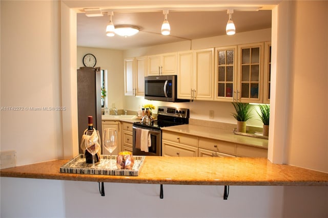 kitchen featuring light stone counters, a sink, stainless steel appliances, glass insert cabinets, and a kitchen bar