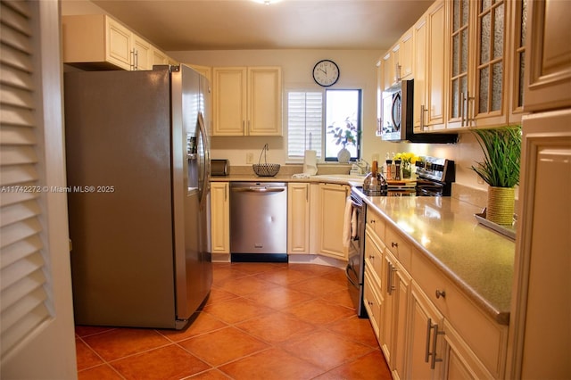 kitchen with light countertops, light tile patterned floors, glass insert cabinets, and appliances with stainless steel finishes