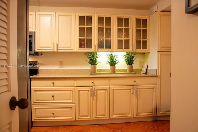 kitchen with tile patterned flooring, stainless steel microwave, glass insert cabinets, and light countertops