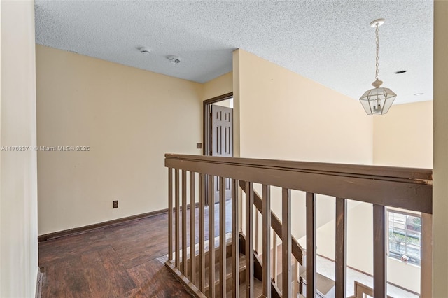 corridor featuring an upstairs landing, baseboards, a textured ceiling, and wood finished floors