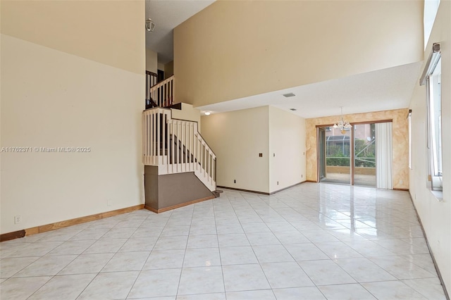 empty room featuring light tile patterned floors, stairway, baseboards, and a towering ceiling