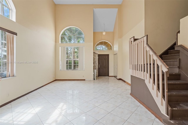 tiled foyer entrance featuring baseboards, a high ceiling, and stairs