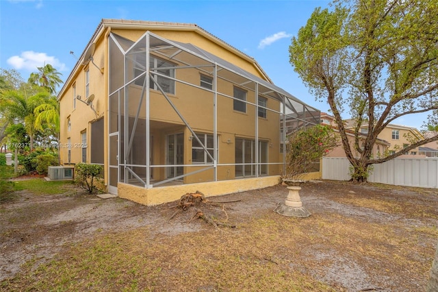 rear view of house with a lanai, fence, and stucco siding