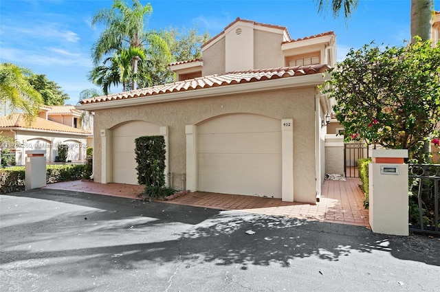 mediterranean / spanish-style home with a tile roof, fence, a garage, and stucco siding