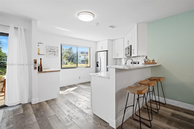 kitchen featuring dark wood finished floors, white cabinets, appliances with stainless steel finishes, and a kitchen breakfast bar