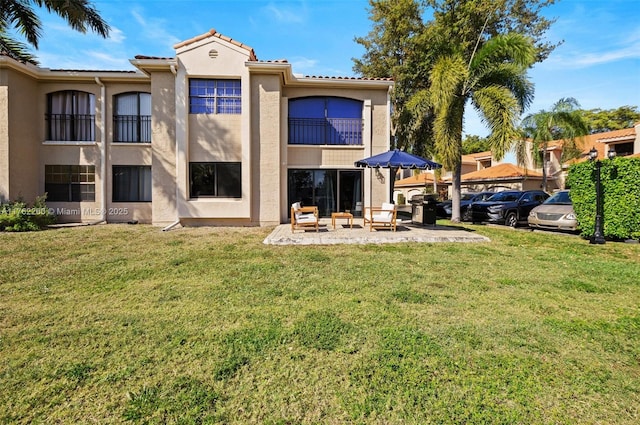 back of house with a tiled roof, stucco siding, a balcony, a yard, and a patio