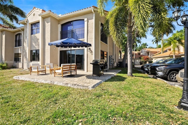 back of property with stucco siding, a lawn, a balcony, and a patio area