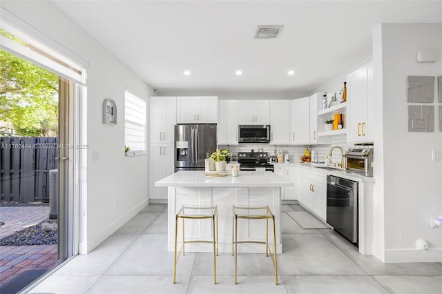 kitchen featuring a kitchen island, open shelves, a sink, decorative backsplash, and stainless steel appliances