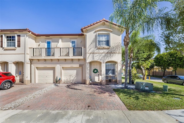 mediterranean / spanish house with a garage, stucco siding, decorative driveway, and a balcony