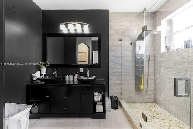 full bathroom featuring double vanity, tile patterned floors, a stall shower, and a sink