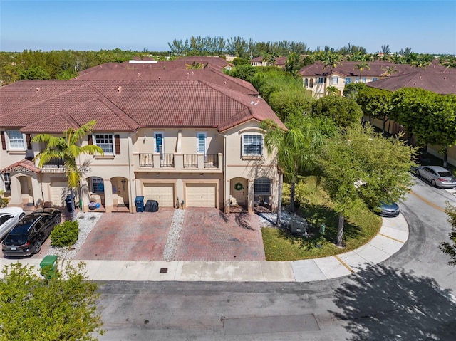 view of front of home featuring stucco siding, a balcony, an attached garage, and a tiled roof