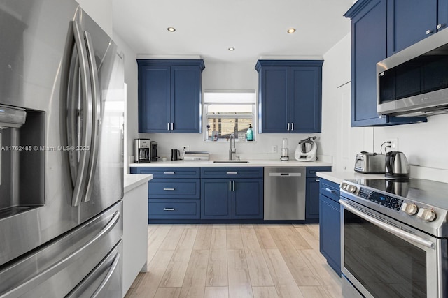 kitchen with blue cabinetry, stainless steel appliances, light countertops, and a sink