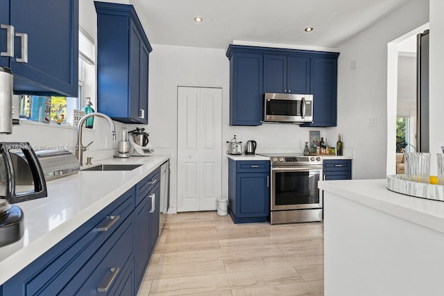 kitchen featuring a sink, blue cabinetry, light wood-style floors, appliances with stainless steel finishes, and light countertops