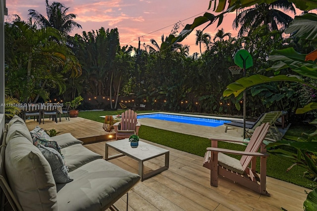 pool at dusk with an outdoor living space, an outdoor pool, a lawn, and a deck