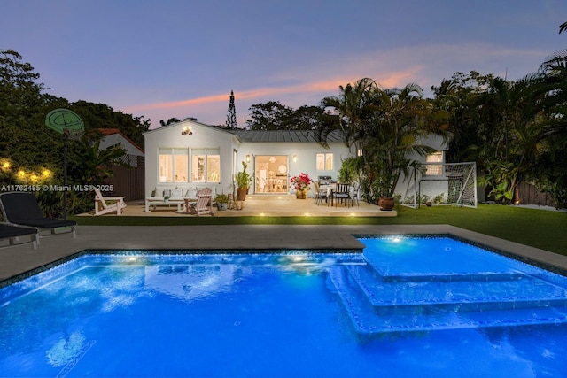 pool at dusk with an outdoor pool, a patio, and a lawn