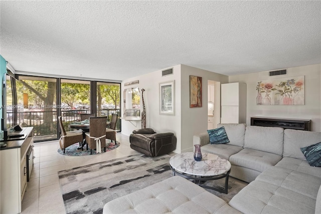 living area featuring a textured ceiling, light tile patterned floors, visible vents, and expansive windows