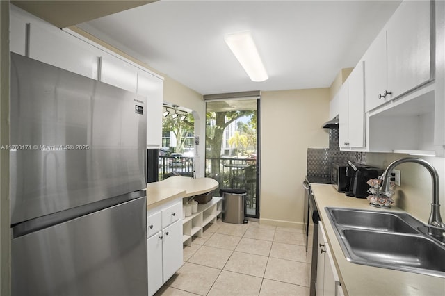 kitchen featuring light tile patterned flooring, freestanding refrigerator, a sink, light countertops, and backsplash