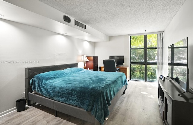 bedroom featuring a wall of windows, wood finished floors, visible vents, and a textured ceiling