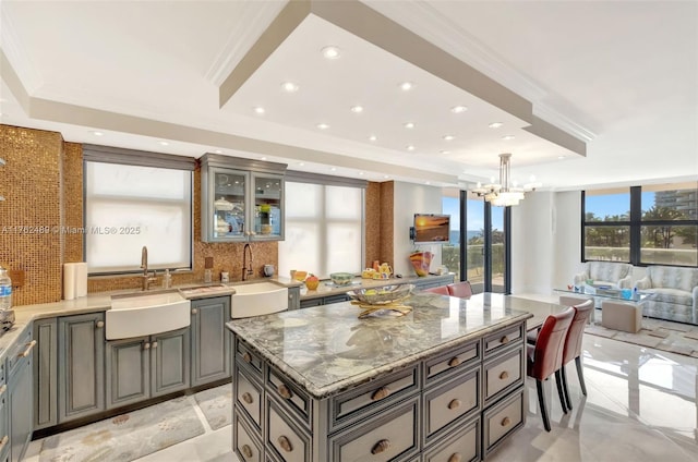 kitchen featuring light stone counters, a sink, crown molding, a raised ceiling, and tasteful backsplash