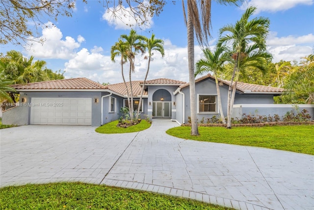 mediterranean / spanish-style house featuring a tile roof, a front yard, stucco siding, decorative driveway, and a garage