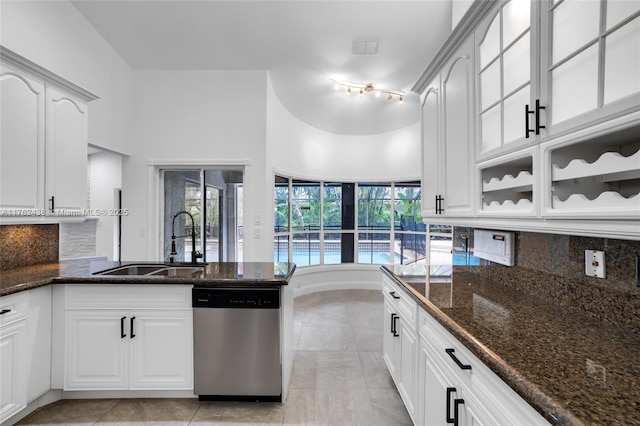 kitchen with dishwasher, decorative backsplash, dark stone countertops, a peninsula, and a sink