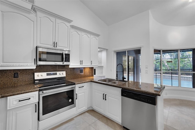 kitchen with a sink, stainless steel appliances, a peninsula, light tile patterned flooring, and lofted ceiling