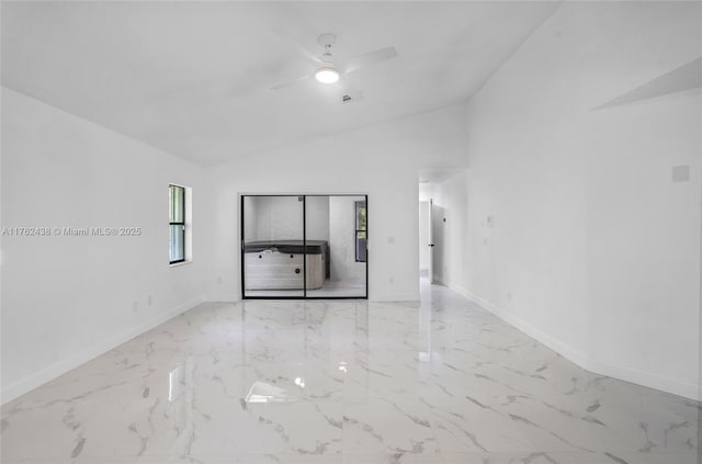 empty room with lofted ceiling, a ceiling fan, marble finish floor, and baseboards