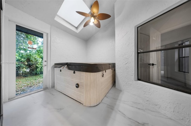 interior space with vaulted ceiling with skylight, marble finish floor, ceiling fan, and a textured wall