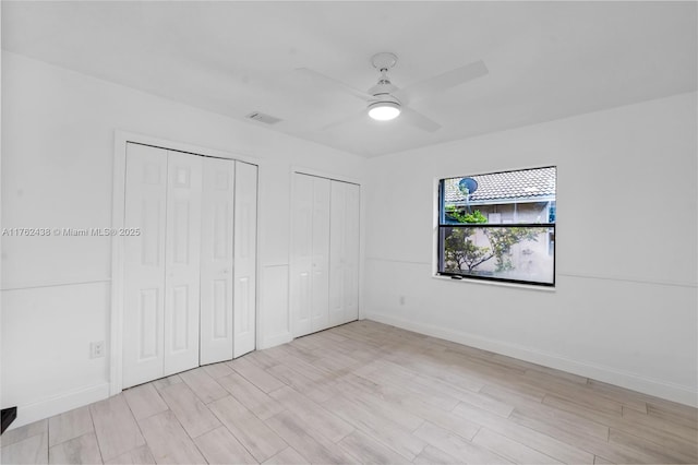 unfurnished bedroom featuring visible vents, baseboards, multiple closets, light wood-style flooring, and a ceiling fan