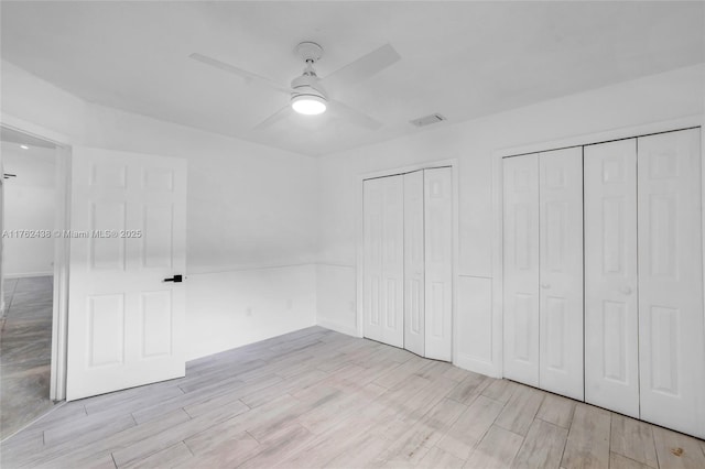 unfurnished bedroom with wood finish floors, visible vents, multiple closets, and a ceiling fan