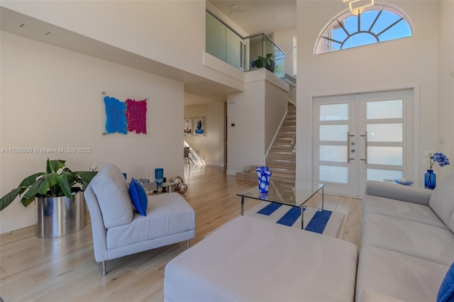 living room with light wood finished floors, stairway, french doors, and a towering ceiling