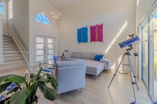 living room with a towering ceiling, french doors, light wood-style flooring, and stairs